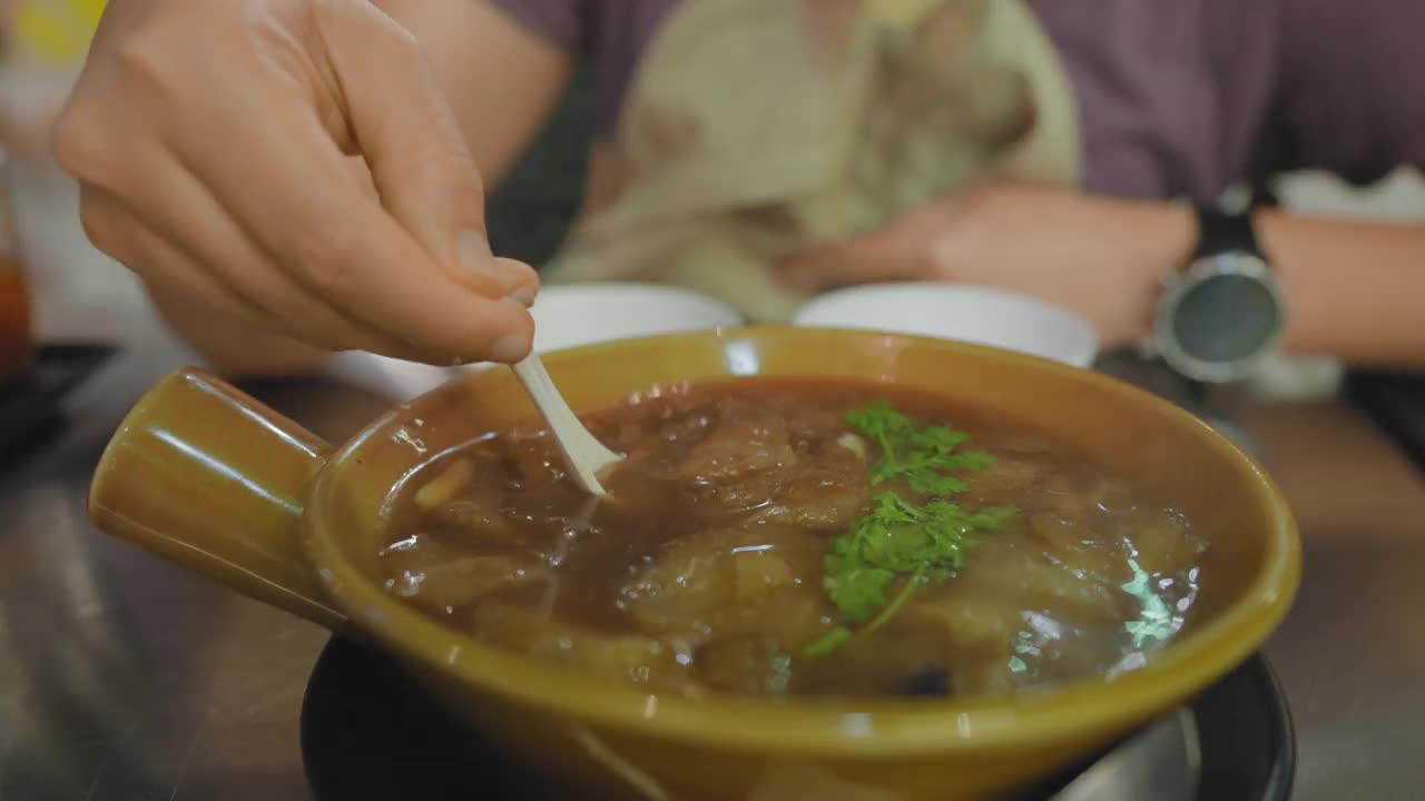 在曼谷唐人街耀拉瓦的一家街头小吃店，在金属桌子上用塑料勺盛着热腾腾的鱼肚汤。用美味的食物跟随手视频下载
