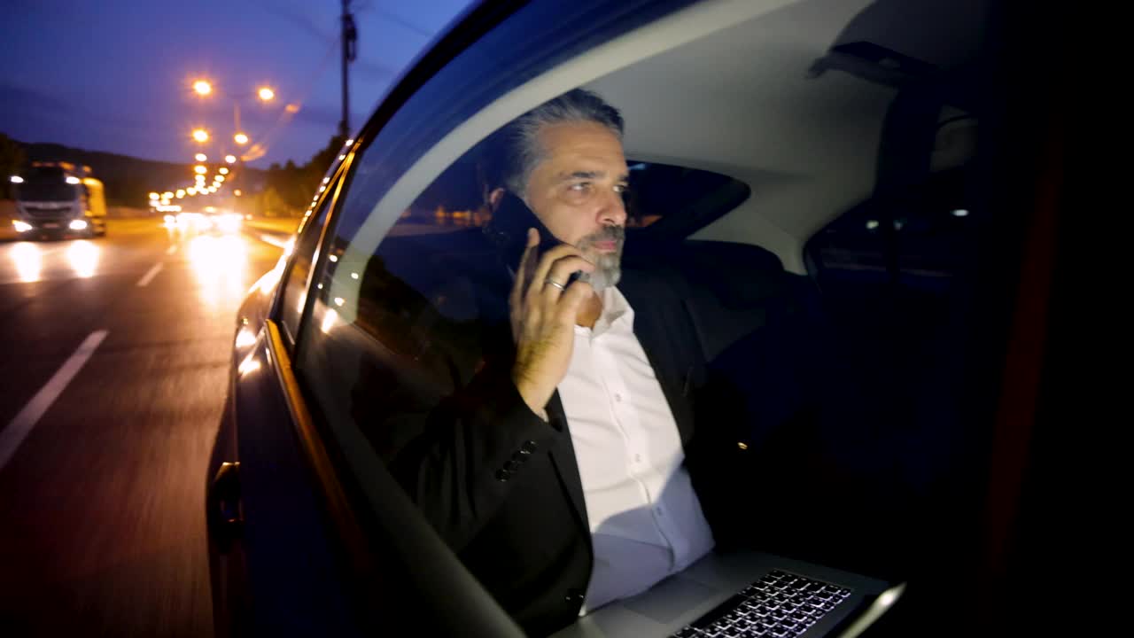 一个灰白头发和胡子的现代成熟男人在汽车里通过电话交谈视频素材