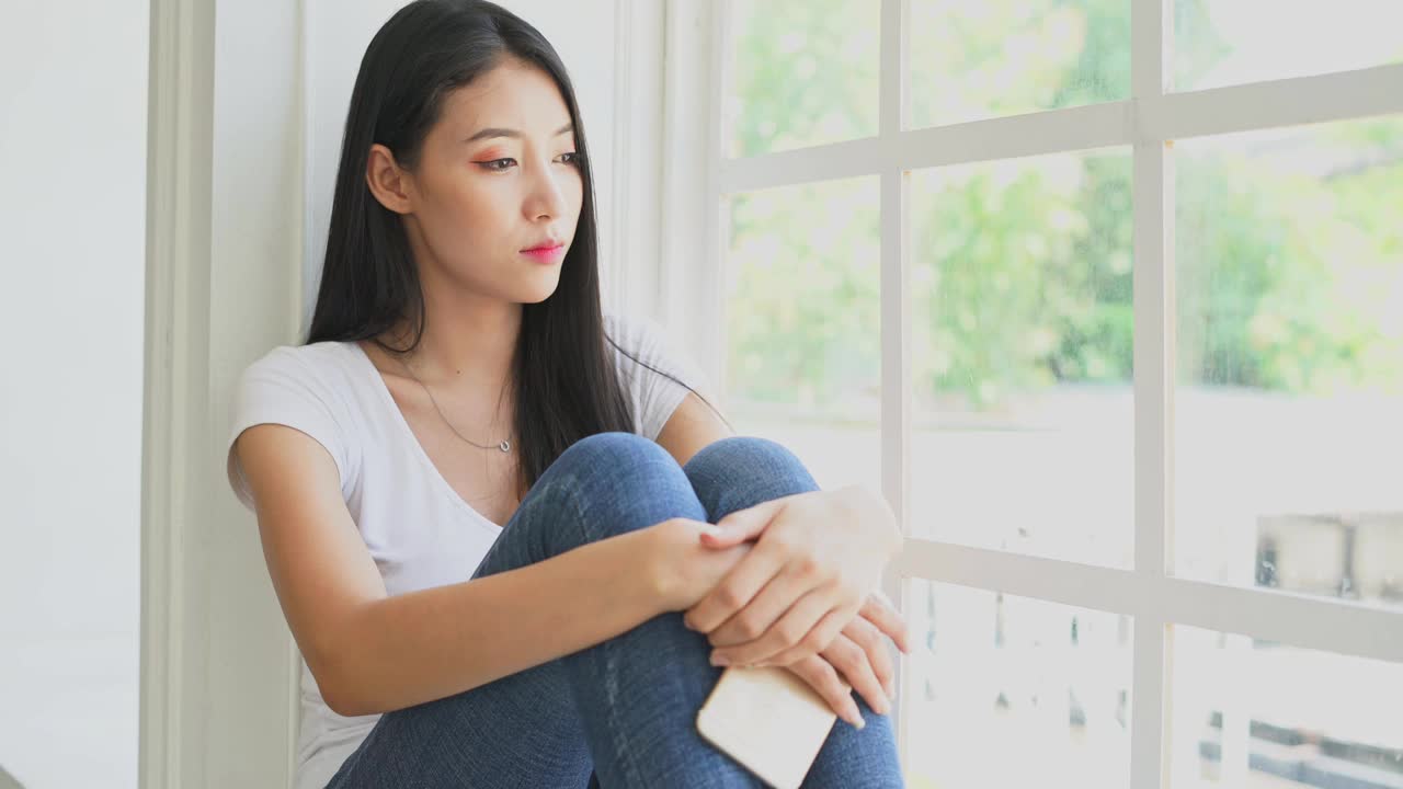 沮丧的女性坐在地板上，亚洲女性望向窗外视频素材