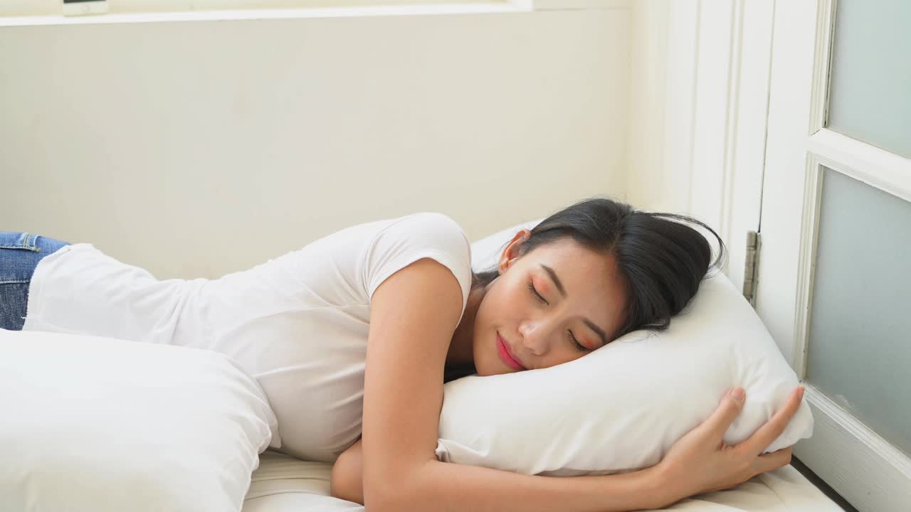 亚洲妇女穿着白色睡衣躺在床上的白色枕头在卧室视频素材