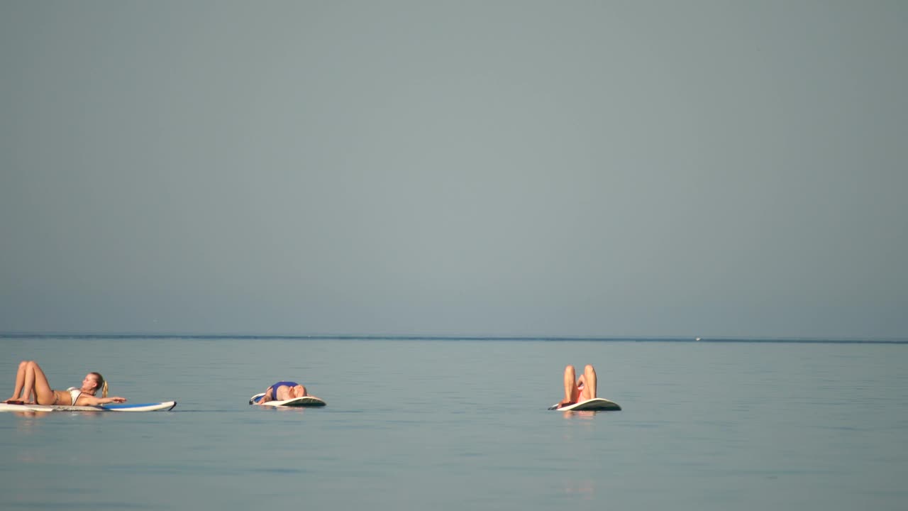 清晨，一群身着泳装的年轻女子在平静的海面上做瑜伽。平衡姿势-健康生活和身心发展之间的自然平衡的概念视频素材