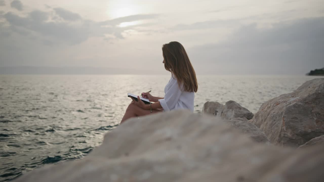 年轻女子坐在沙滩上写笔记本视频素材