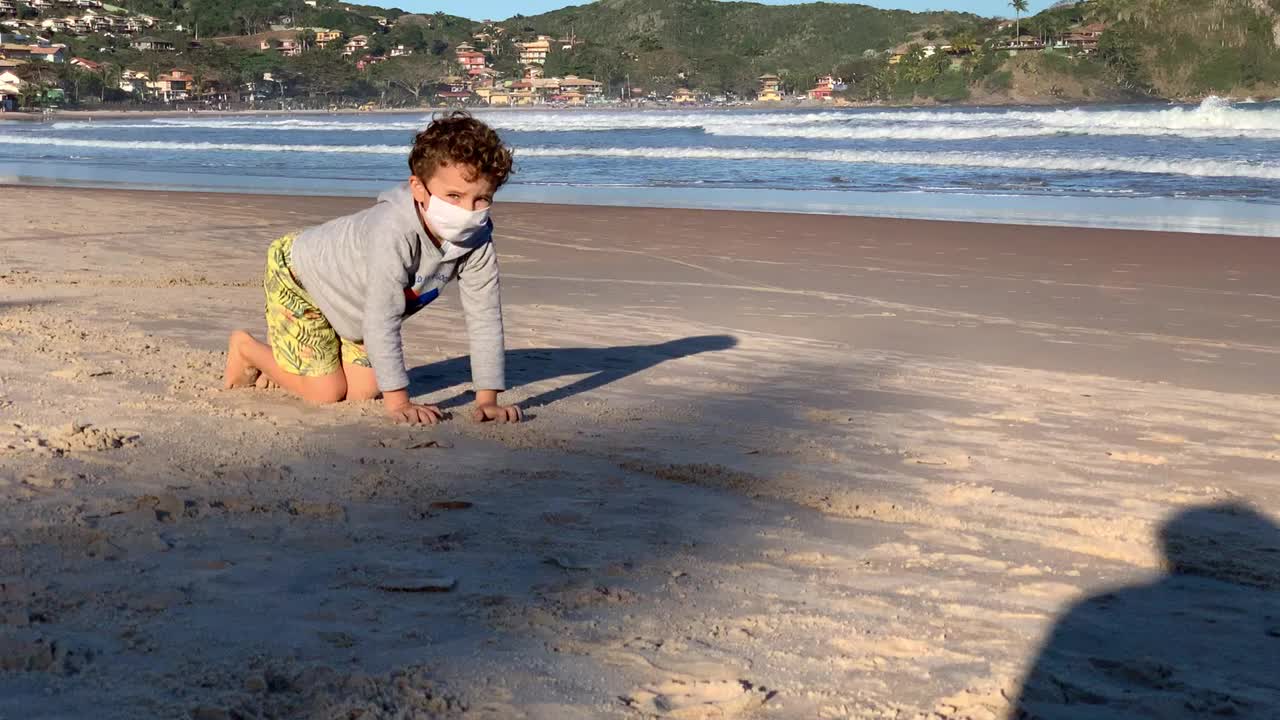 满身是沙戴着口罩的脏男孩在海滩上爬行视频下载