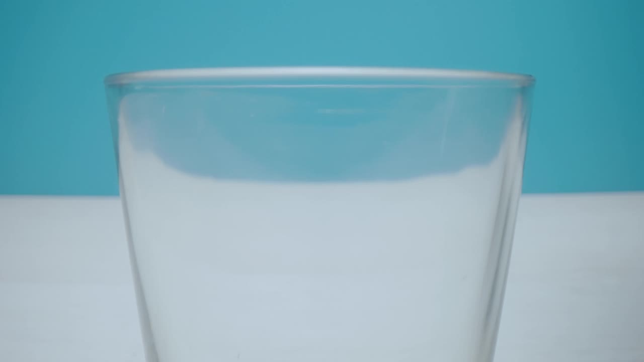 牛奶被倒进一个牛奶玻璃杯，背景是蓝色的。视频下载