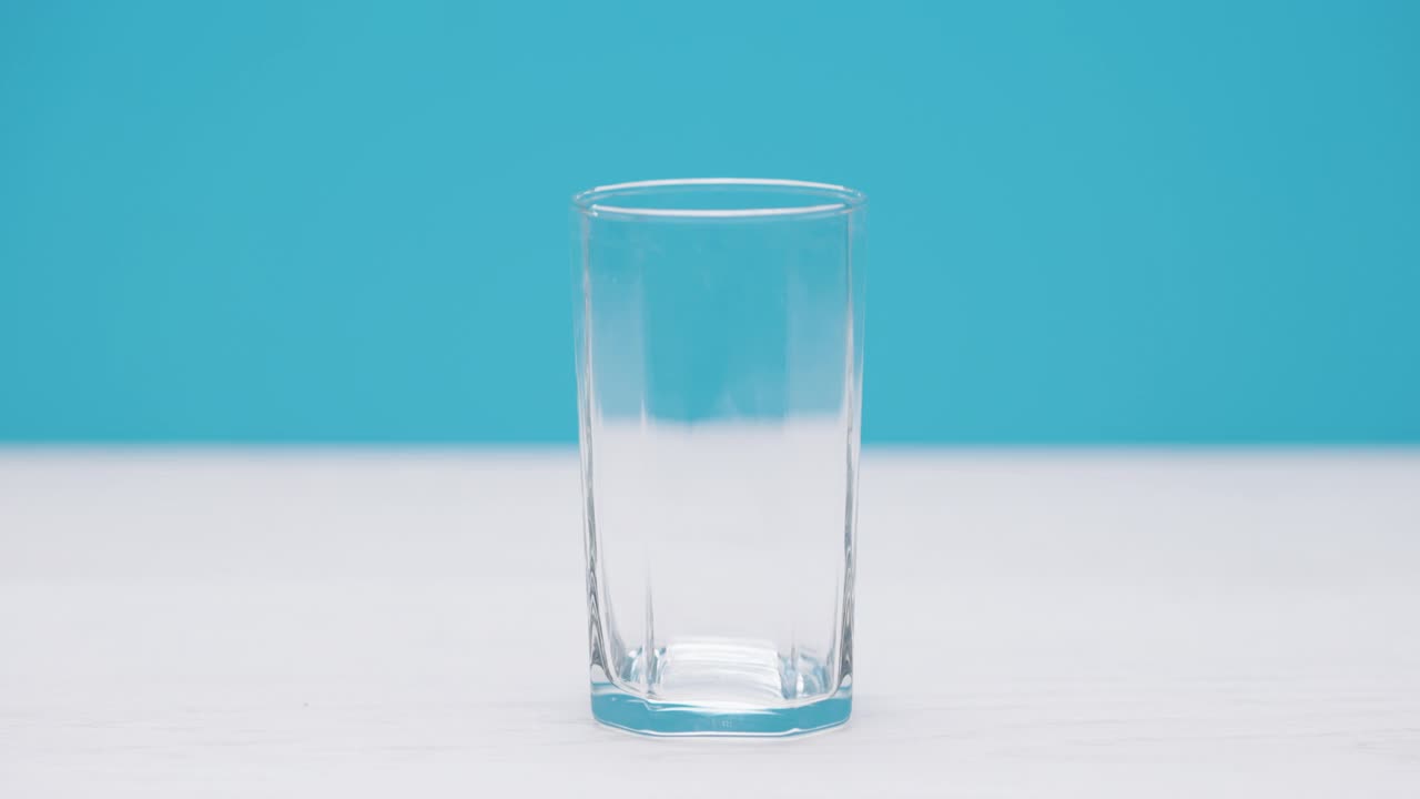牛奶被倒进一个牛奶玻璃杯，背景是蓝色的。视频素材