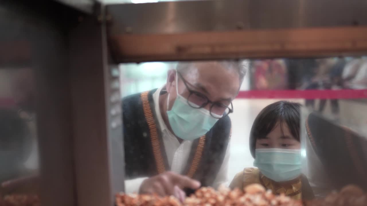亚洲华人爷爷孙女看着快餐工人把爆米花舀到纸桶里，在娱乐大楼电影院电影院电影院视频素材