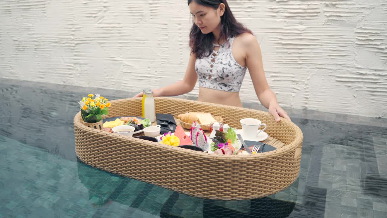 漂浮早餐亚洲女孩在泳池边吃早餐。视频下载
