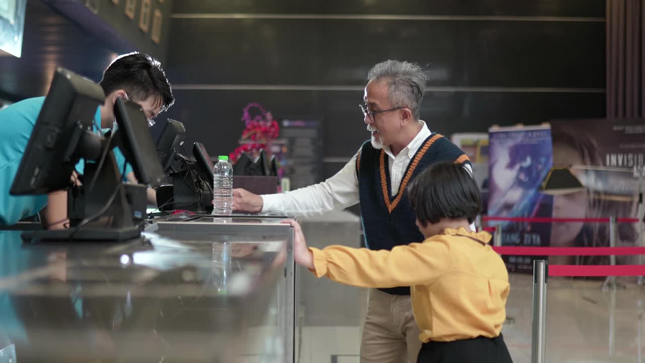 亚洲的中国爷爷孙女在电影院放映前用非接触式付款购买爆米花视频素材