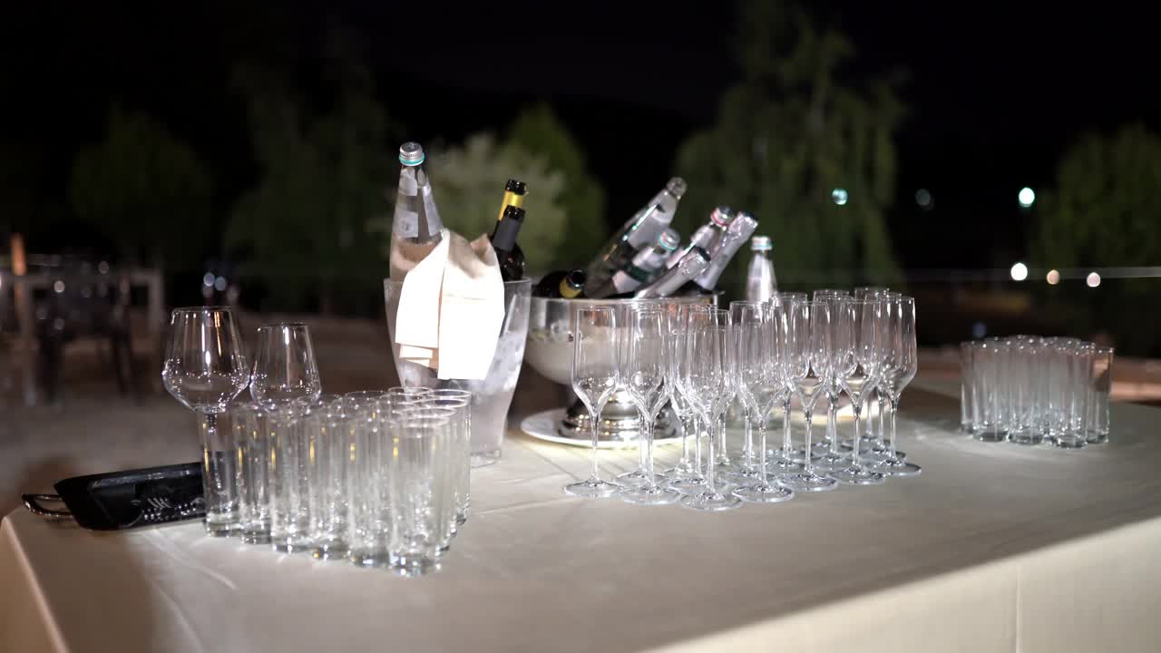 户外装饰的自助餐桌上摆放着透明的水晶高脚杯和水杯，还有两个装满冰和香槟或红酒的银桶，为庆祝活动准备的宴会桌视频素材