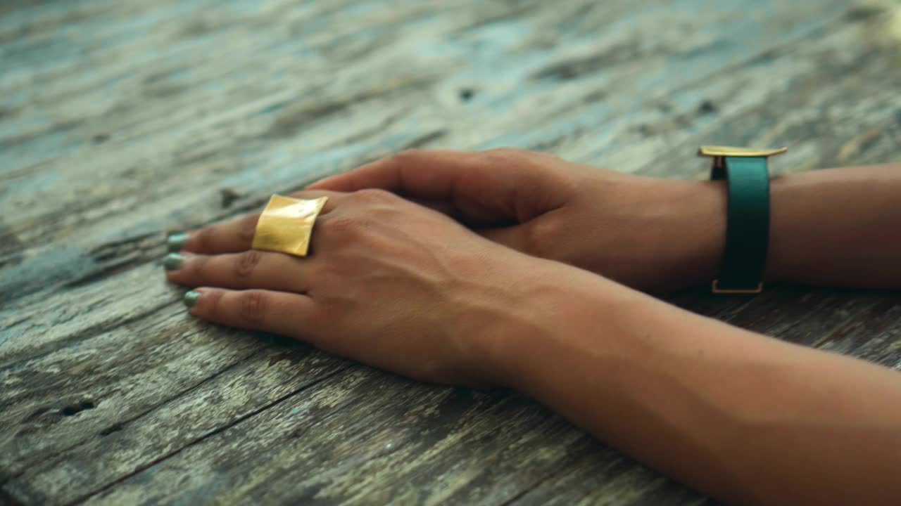 一个欧洲女孩坐在一张木桌旁，把手放在他身上，手上戴着金戒指和手表视频素材