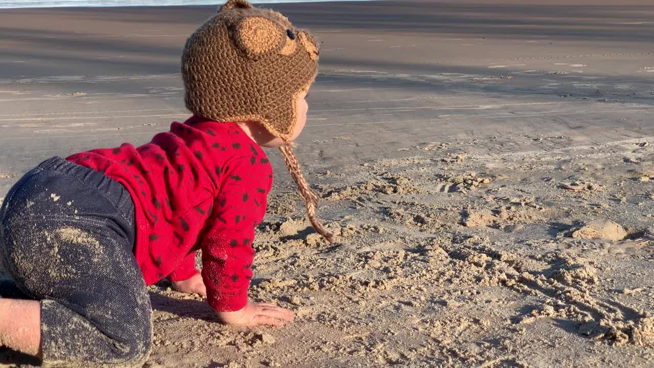 小女孩浑身是沙，戴着针织帽坐在沙滩上视频下载