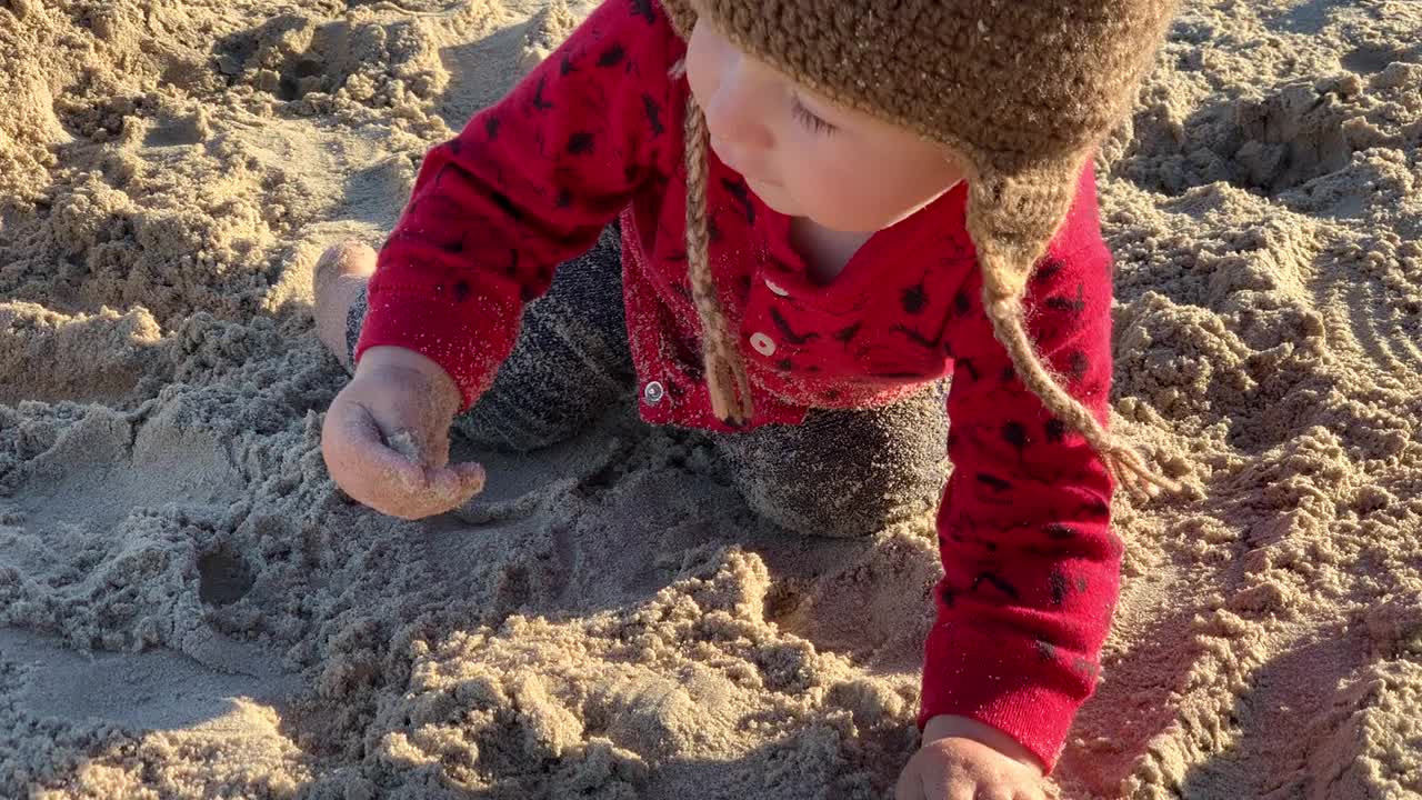 脏兮兮的小女孩戴着针织帽在沙滩上玩沙子视频下载