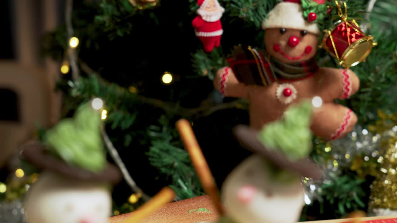 照片:在一间装饰着圣诞树的公寓里，有两个自制的冰霜雪人杯形蛋糕，用冰霜球做的，黑巧克力饼干，绿色奶油做的帽子，粉色的鼻子和巧克力球做的绿色纽扣，椒盐卷饼棒做的手臂视频下载
