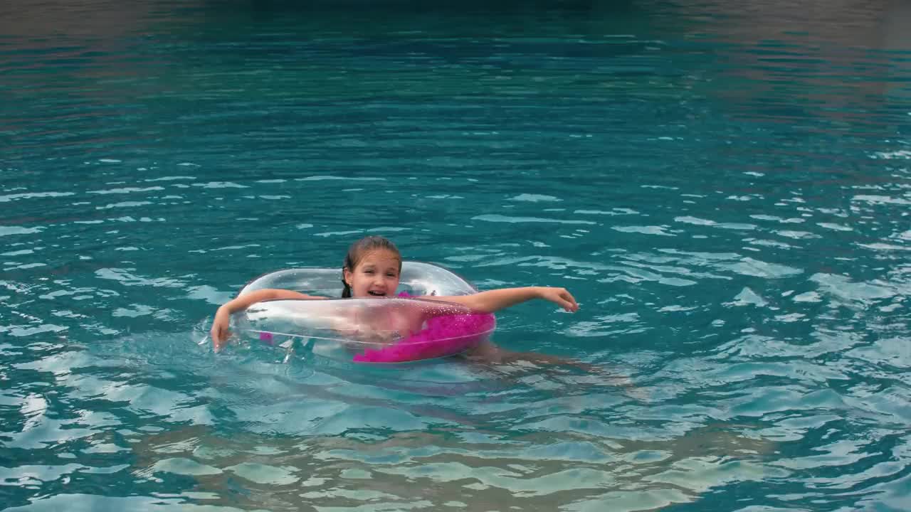 那个可爱的小女孩在游泳池里玩得很开心。孩子们暑假在游泳池里蹦蹦跳跳，打转，泼水。快乐的童年。视频下载
