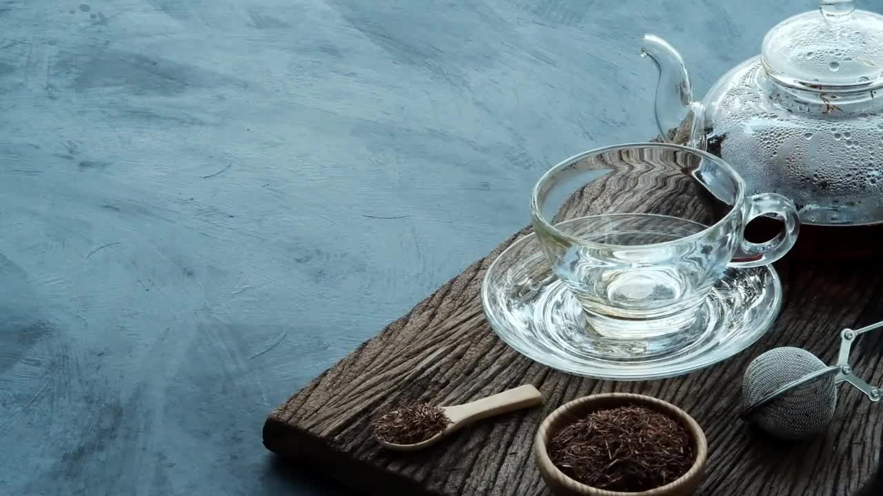 工艺泡茶，将热腾腾的茶水从茶壶倒进茶杯里，放在深色厨房餐桌背景的旧木板上，静物放松时光的深色心情风格。视频素材