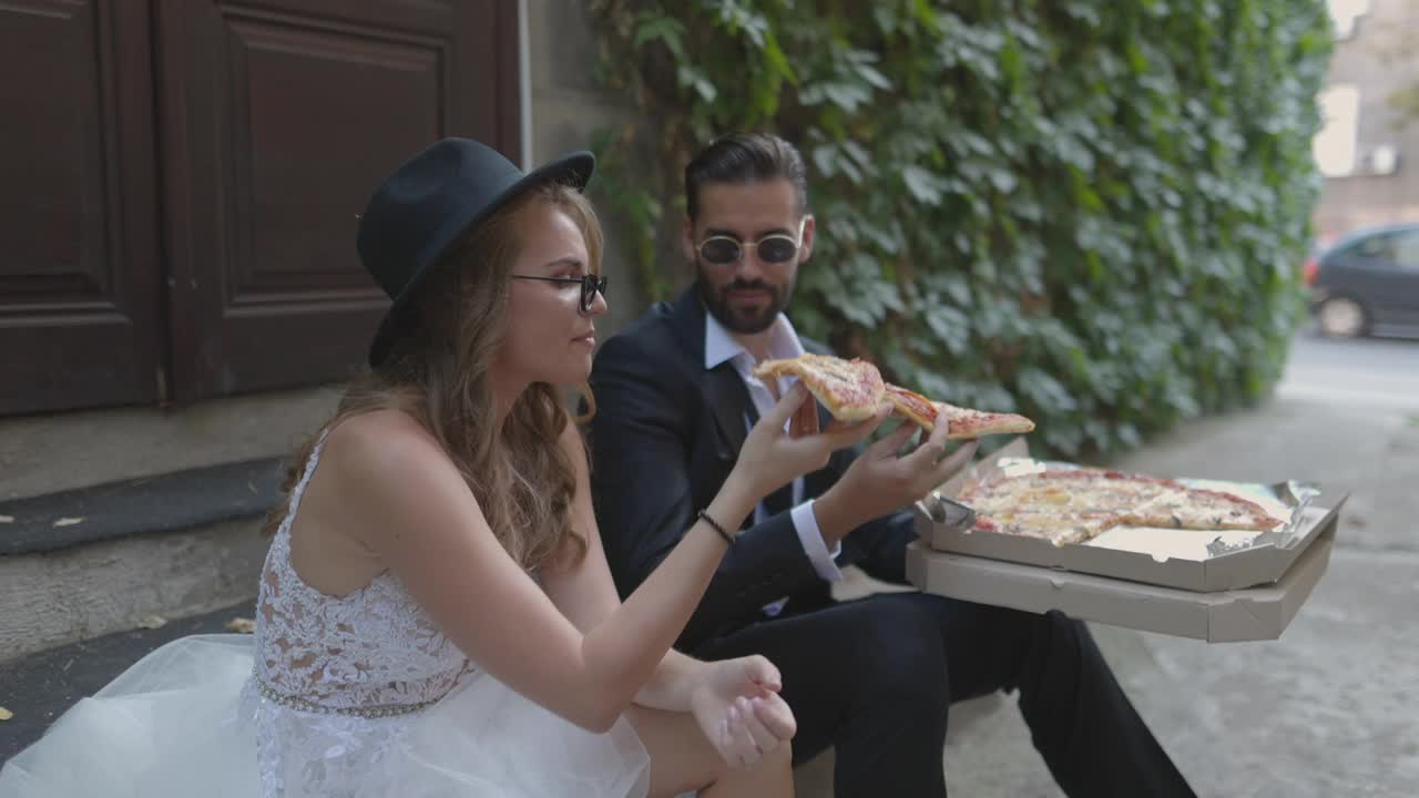 新娘和新郎坐在小巷的楼梯上，一边吃着披萨一边微笑视频下载