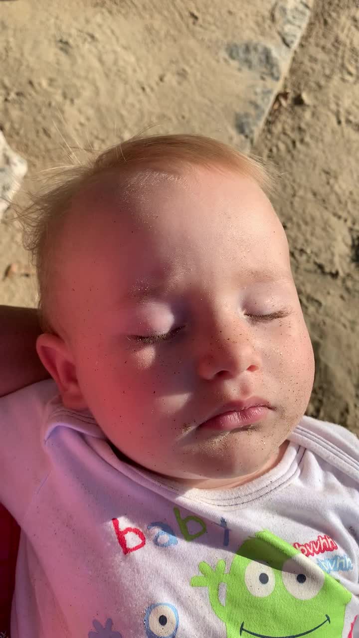 婴儿满脸都是沙子，头发随风飘动，睡在沙滩上视频下载