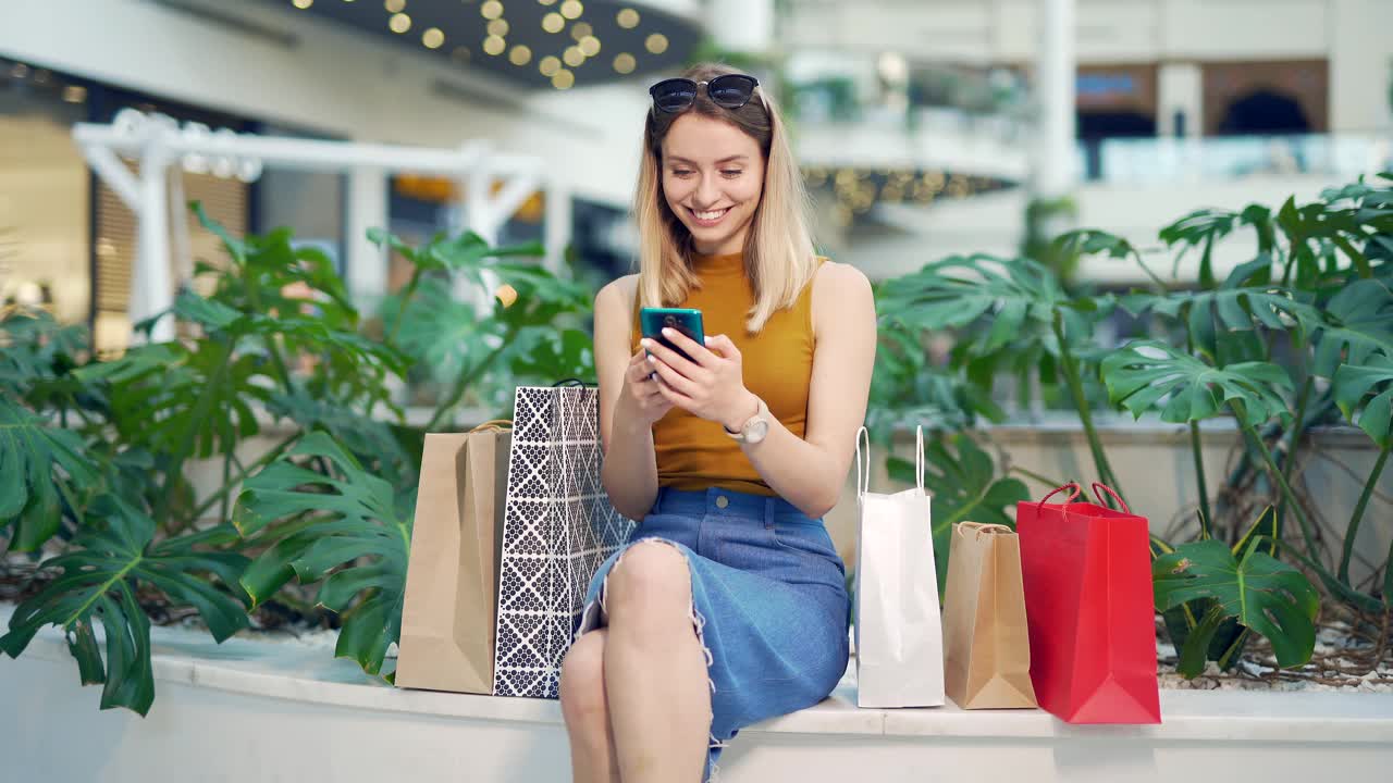 年轻的女性消费者在商场浏览聊天和使用智能手机视频下载