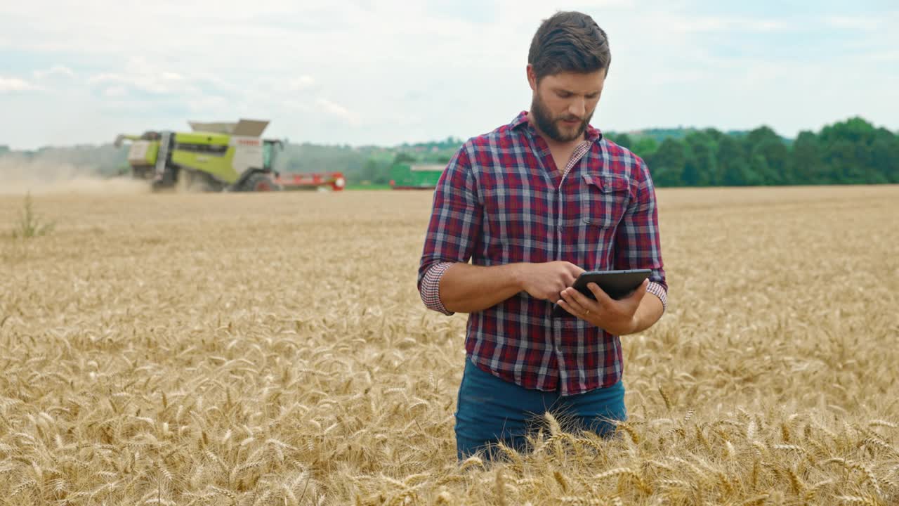 当联合收割机收割小麦时，农夫在麦田中间使用数码平板电脑视频素材