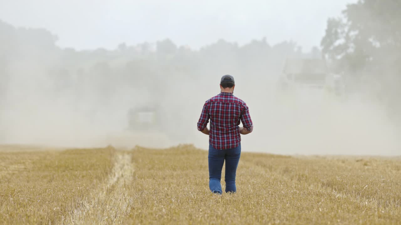一位农民走在联合收割机后面在麦田里收割视频素材