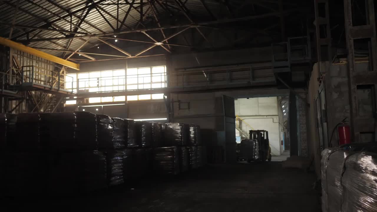 装载机司机在一个非常黑暗的仓库里装卸装有袋子的托盘。建筑材料的大仓库。提灯笼的装载机。视频素材