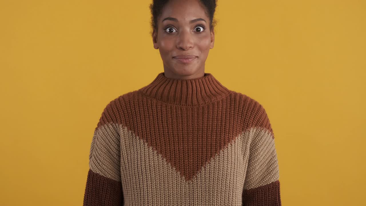 相片的微笑热情的非洲裔美国女孩在舒适的毛衣愉快地看着照相机在黄色的背景视频下载