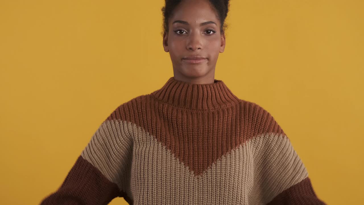 漂亮的非洲裔美国女孩在针织毛衣顽皮地显示和平的姿态在黄色背景视频下载