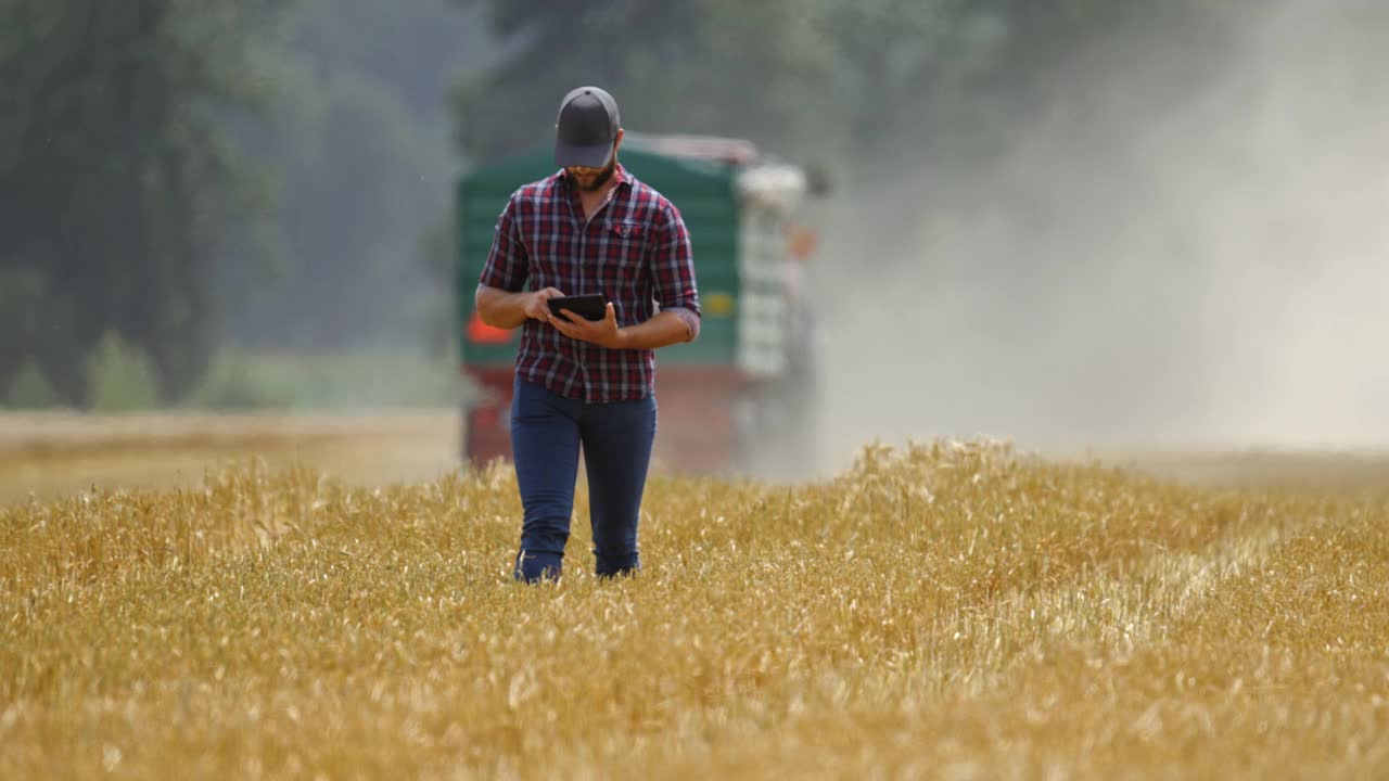 法默(SLO MO Farmer)在田地里走着，身后开着一辆拖拉机视频素材