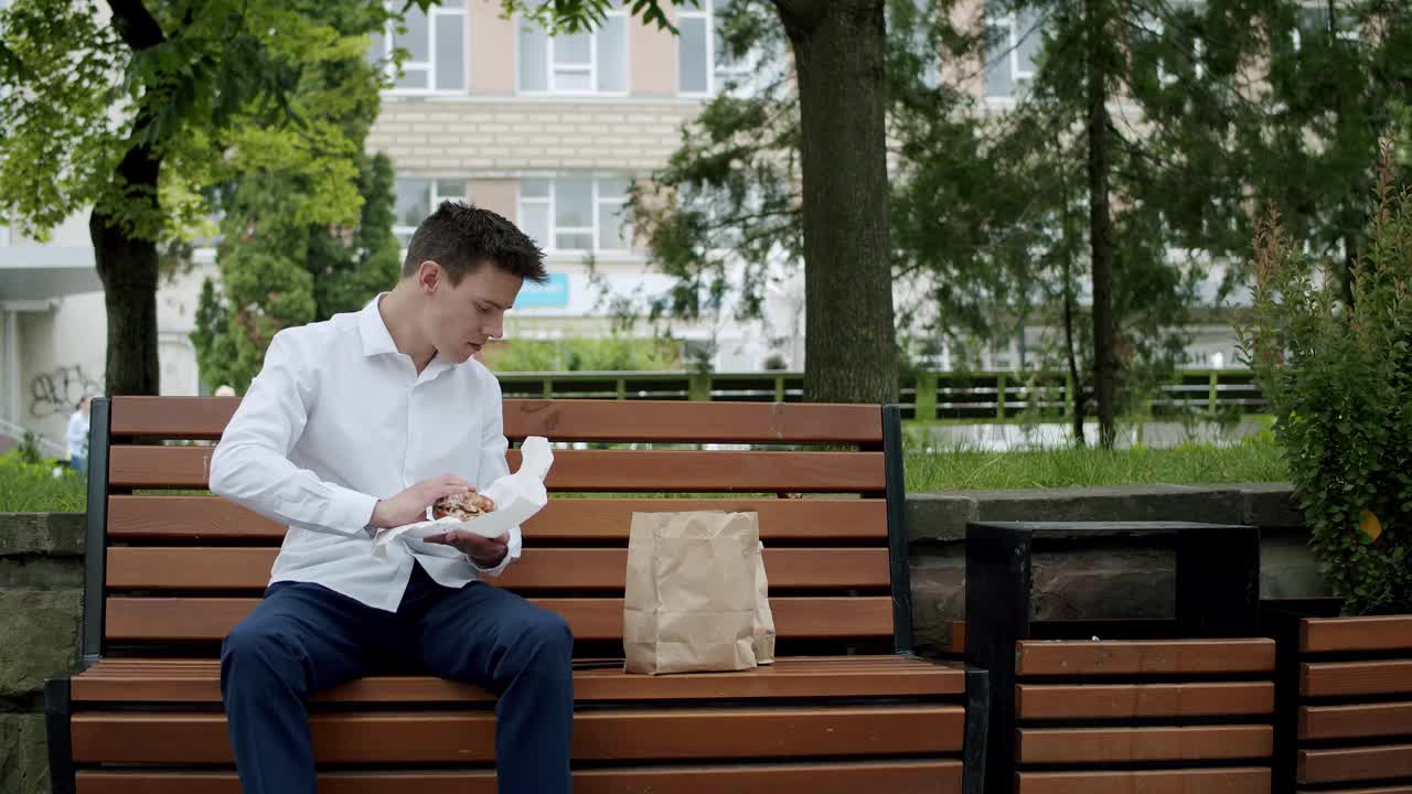 饿了，西装革履的年轻人拿了一个汉堡包，一边打电话一边吃视频素材