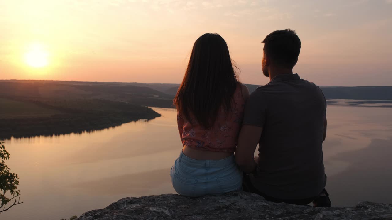 这对年轻夫妇坐在岩石山上，俯瞰着美丽的河流。慢动作视频素材