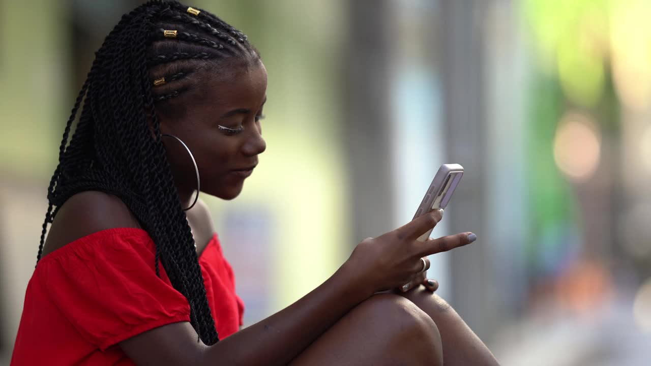 一个坐在人行道上玩智能手机的非洲女人视频素材