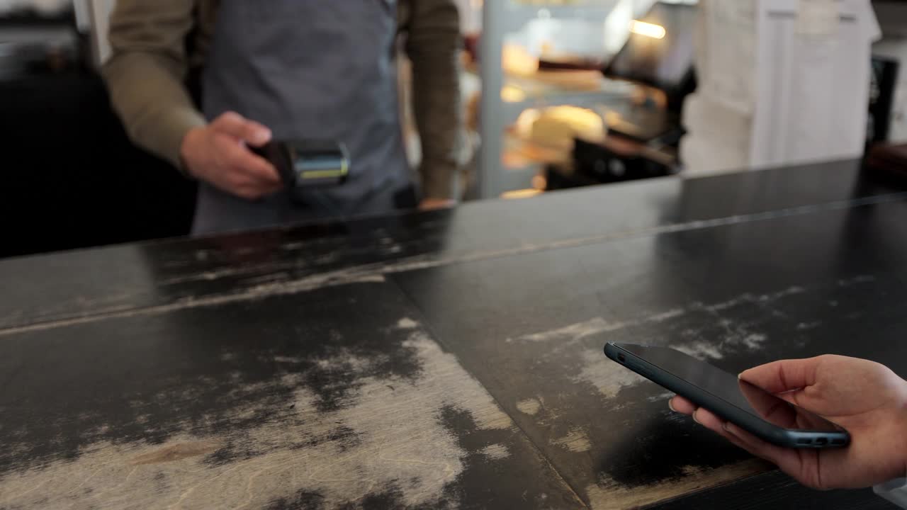 在咖啡馆，一名男子正在为一位顾客制作外卖咖啡，这位顾客通过非接触式手机支付到咖啡馆的信用卡系统，并提供数字交易服务。视频素材
