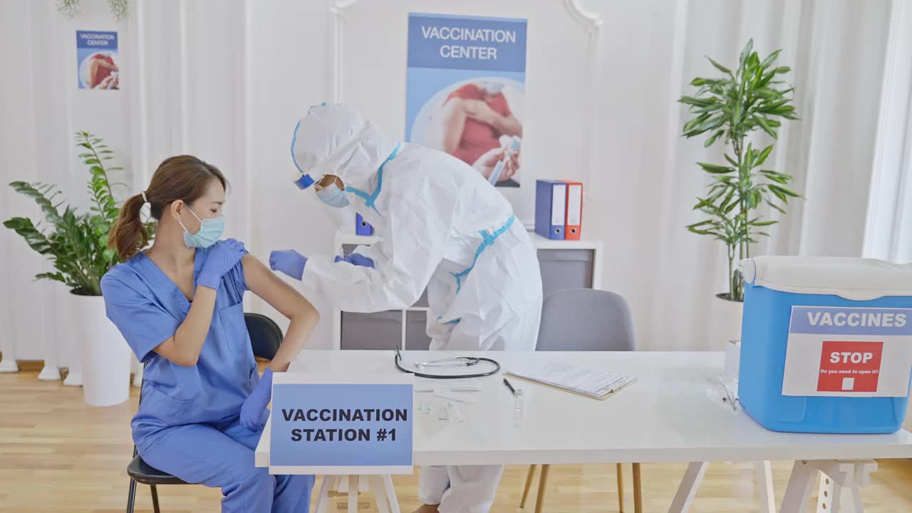 身穿防护服的医护人员在Covid-19疫苗接种中心为女护士接种疫苗视频素材