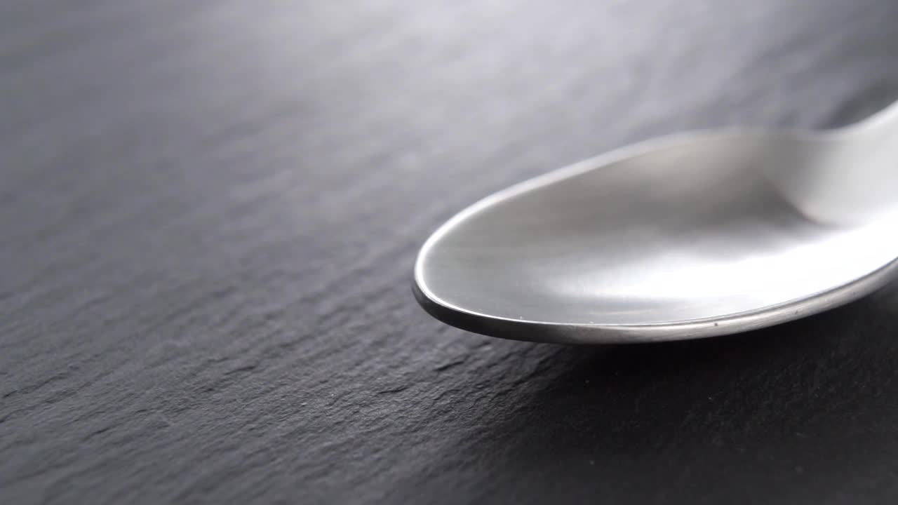干燥的绿茶茶叶落入黑色厨房石板上的金属茶匙中视频下载