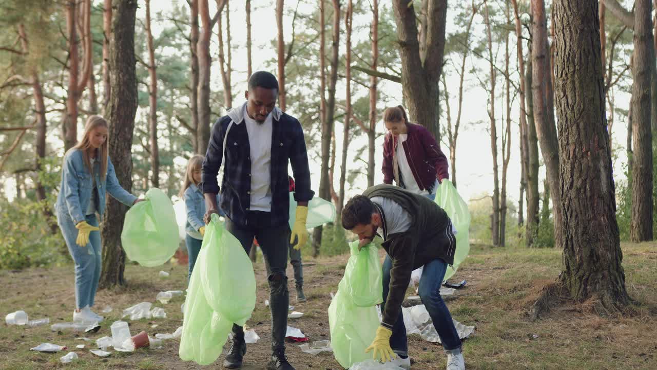 英俊勤劳的多种族男子帮助收集垃圾到塑料袋他们的朋友-自然活动家和给予击掌，社会反对污染的概念视频下载