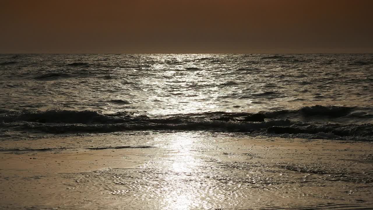 日出时的海岸线景观，太阳在地平线上，海浪拍打着海岸。视频素材