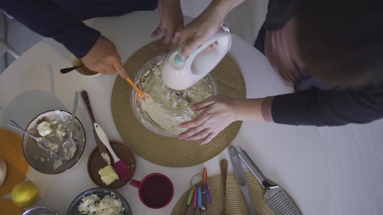 正上方的亚洲华人中成人夫妇在周末在家的餐桌上用电动搅拌器制作奶酪挞蛋糕，准备甜点视频下载
