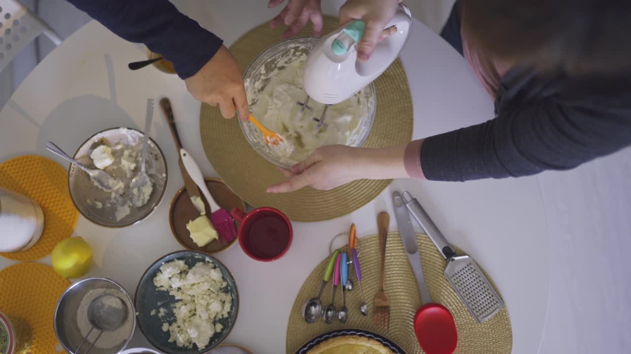 正上方的亚洲华人中成人夫妇在周末在家的餐桌上用电动搅拌器制作奶酪挞蛋糕，准备甜点视频下载