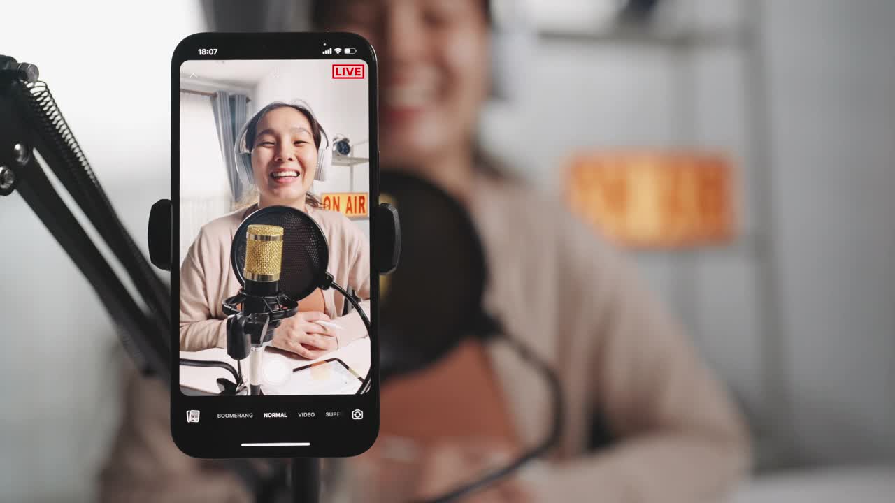 亚洲女性网红使用麦克风戴耳机，用智能手机录制内容，用于在线社交媒体视频下载