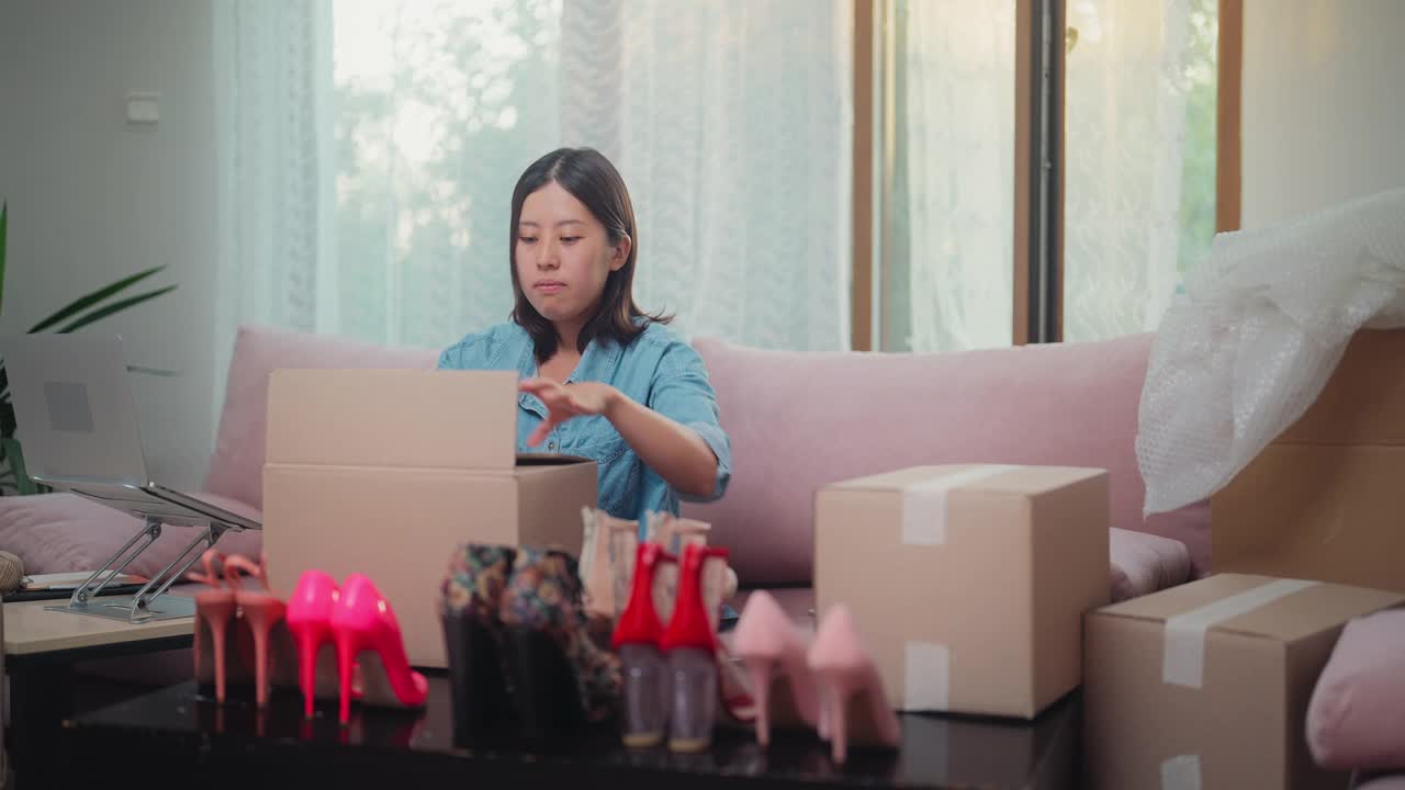 年轻女子在家工作，在网上卖鞋。年轻女子包装鞋子寄给顾客视频下载