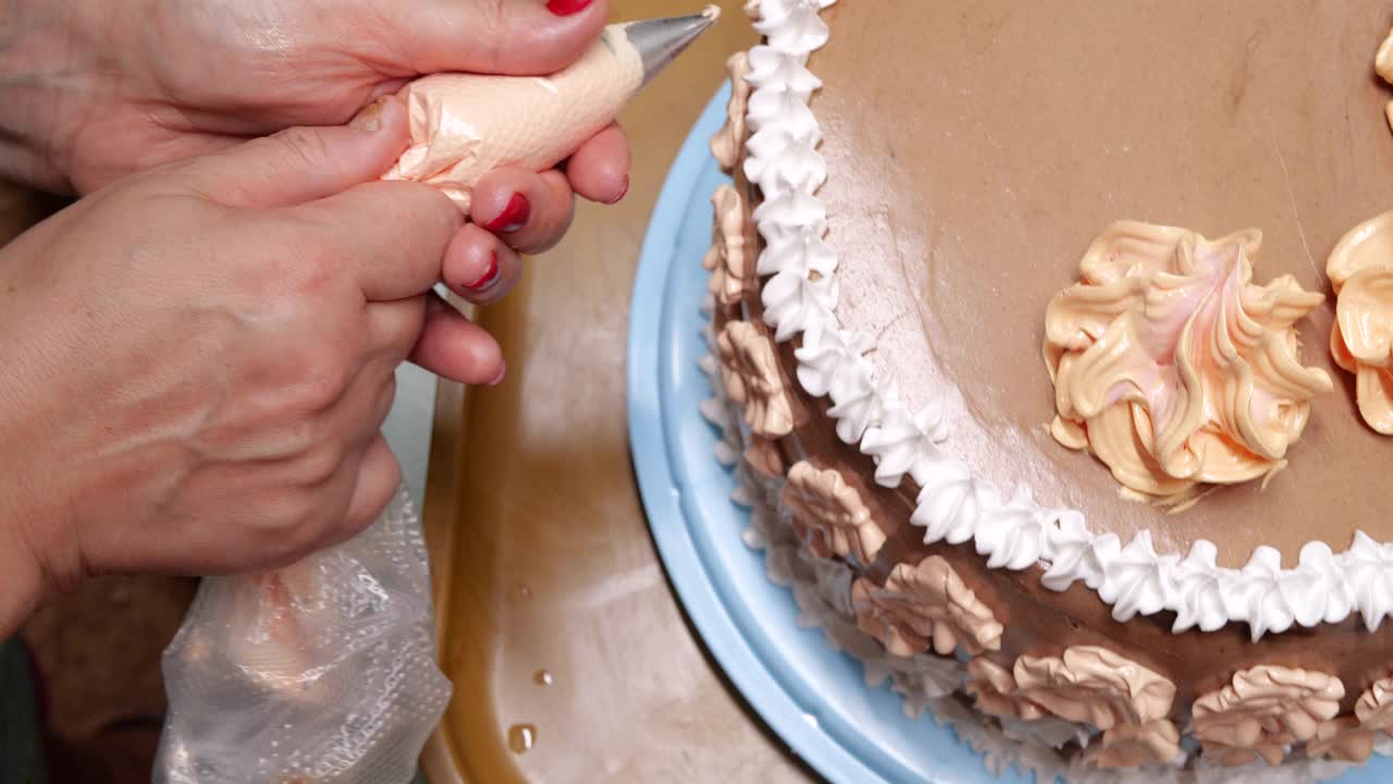 糖果女店员正在用糕点袋往海绵蛋糕上倒奶油，这是特写镜头。糕点师正在做自制的蛋糕。烹饪，烘焙，烹饪，家常菜视频下载
