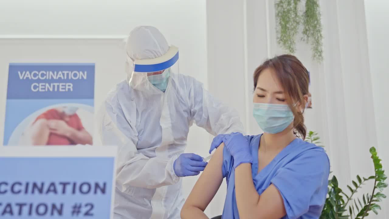 身穿防护服的医护人员在Covid-19疫苗接种中心为女护士接种疫苗视频素材