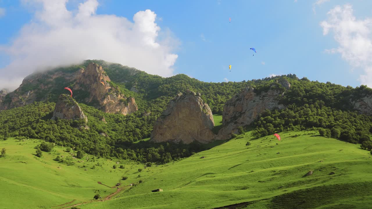 滑翔伞飞行员驾驶滑翔伞在云朵和青山之间飞行。视频素材