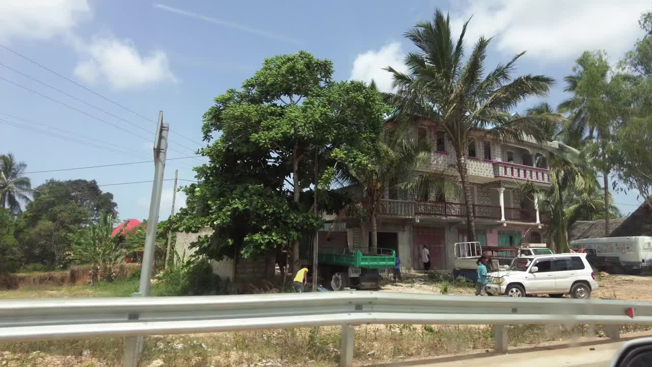 开车经过非洲的贫民窟和村庄，破旧的房子在棕榈树之间视频素材