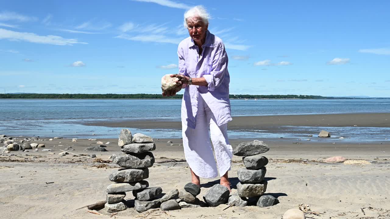 老妇人独自在夏天的海滩上玩石头放松视频下载