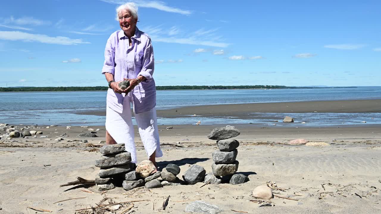老妇人独自在夏天的海滩上玩石头放松视频下载