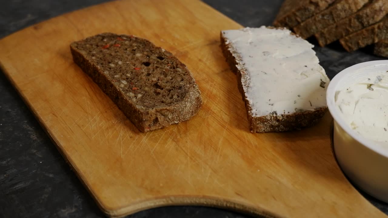 把奶油芝士涂在面包片上。用白软干酪做健康的三明治涂在黑麦面包上的奶油芝士。视频素材