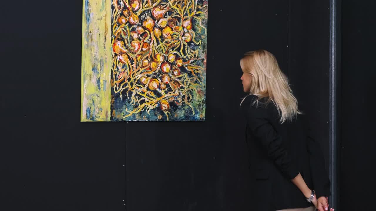 一个年轻的金发女人在画廊里看现代艺术家的画视频素材