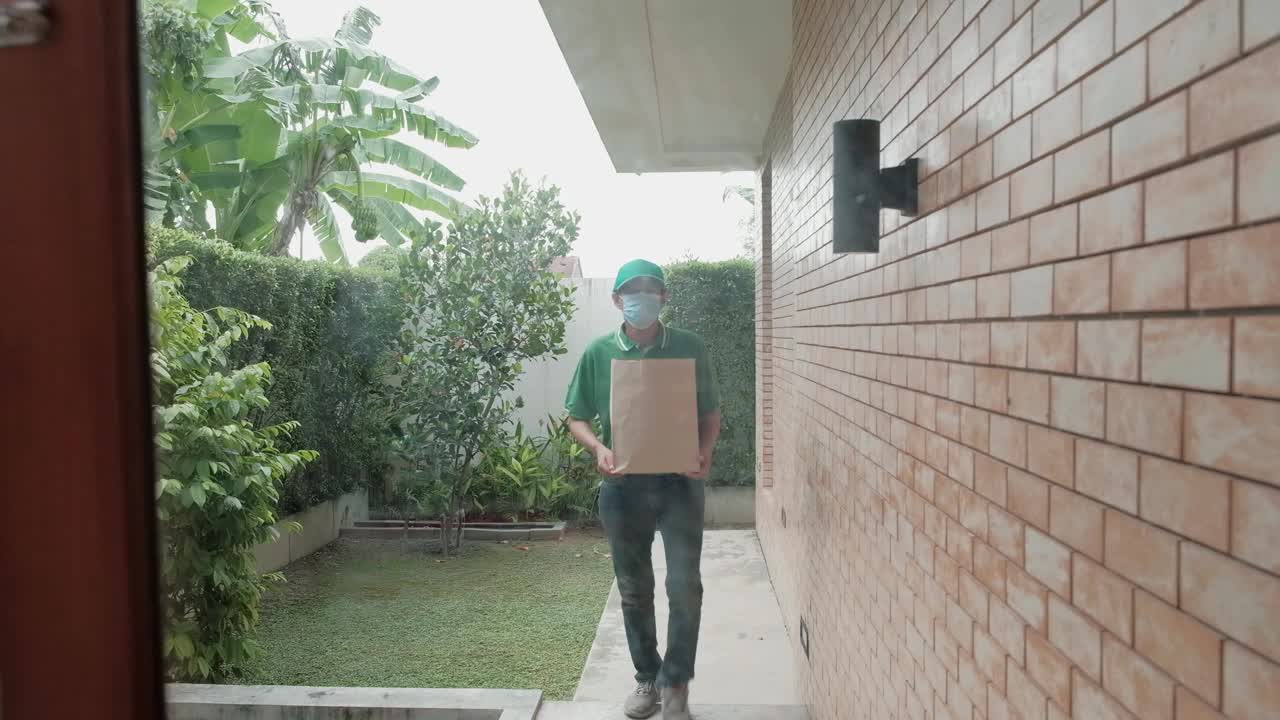 戴口罩的快递员将包裹交给一名亚洲妇女。视频素材