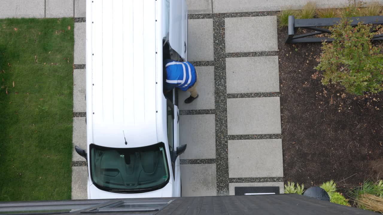 从头顶拍摄的男性送货司机将包裹从货车上卸下，然后将农产品箱搬到家的前门视频下载